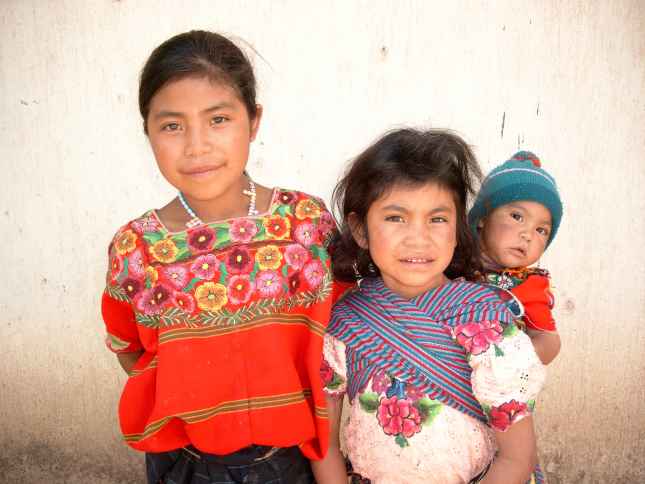 Drei Geschwister in Lateinamerika. Der kleine Bruder wird im Tragetuch auf dem Rücken getragen.