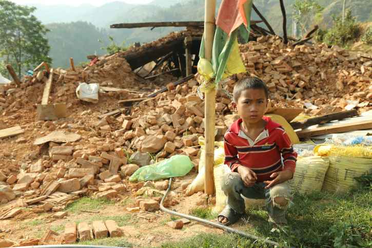 Nach dem Erdbeben in Nepal sitzt ein Junge vor einem zerstörten Haus.