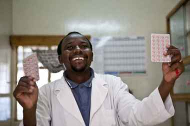 A tanzanian pharmacist holds two blister packs aloft. 
