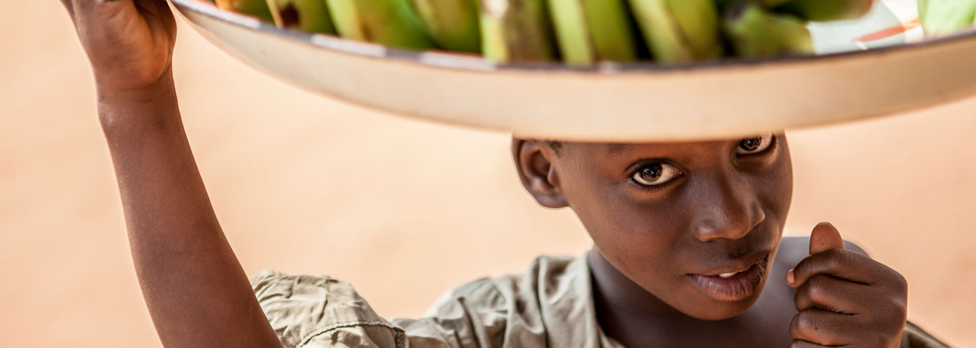 Der togoische Junge trägt eine Schale mit Bananen.