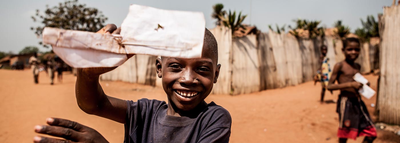 Der Junge im Projekt in Togo hat einen Papierflieger gefaltet und zeigt ihn in die Kamera.