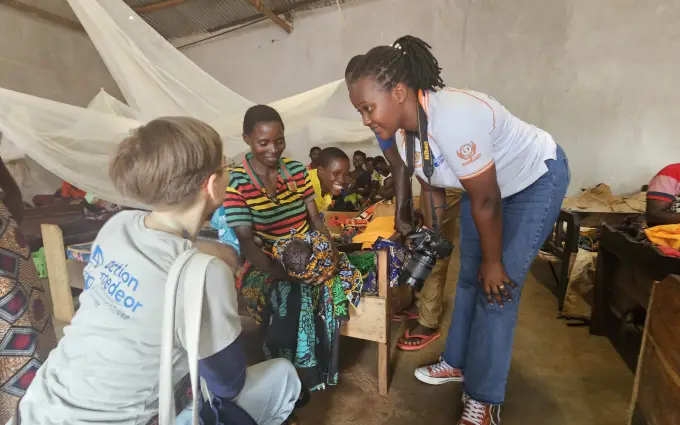 An action medeor staff member is kneeling in front of a mother with a baby.