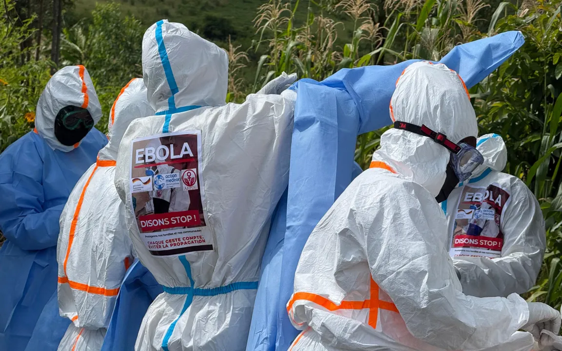 Eine Person mit einem Ebola-Schutzanzug zieht sich einen Schutzkittel über.
