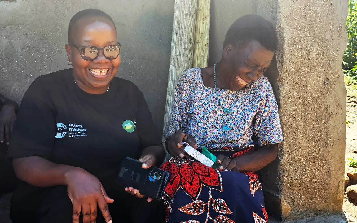 A younger and an older woman, who holds medicine in her hands, are smiling. 