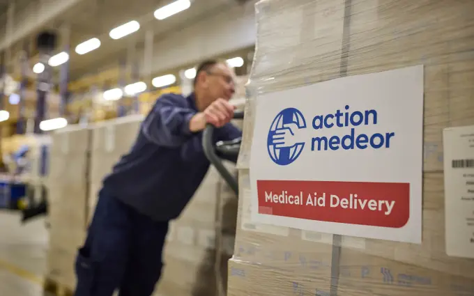 Ein Mann schiebt eine Palette mit Paketen mit der Aufschrift "action medeor Medical Aid Delivery".