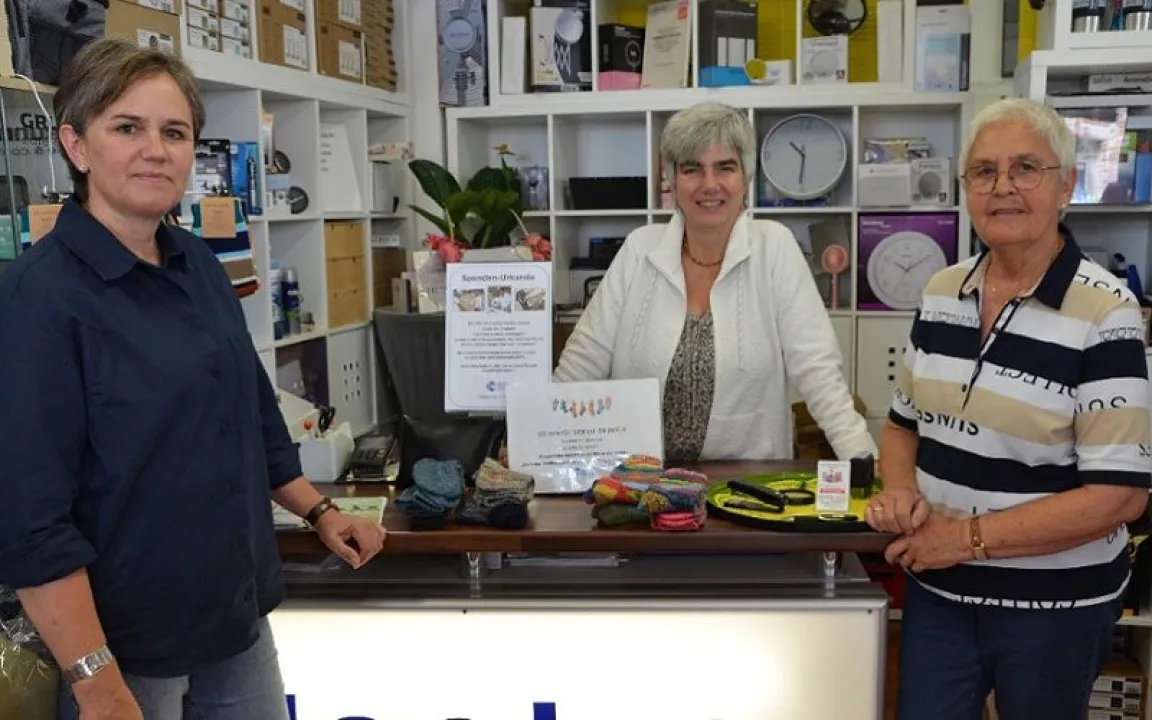Three women are standing at a sales counter.